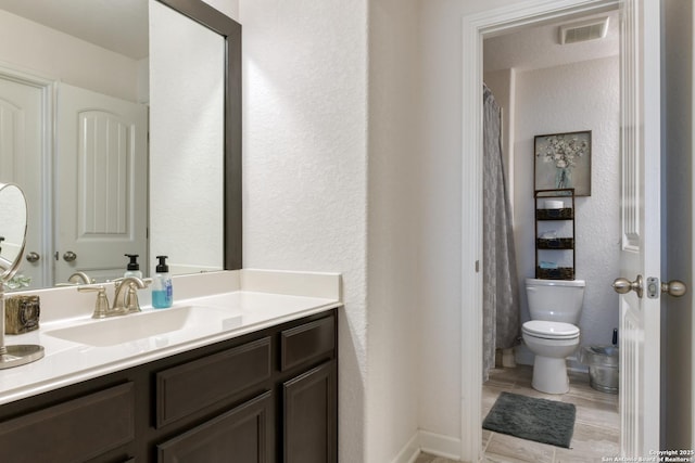 bathroom featuring toilet, a textured wall, visible vents, and vanity