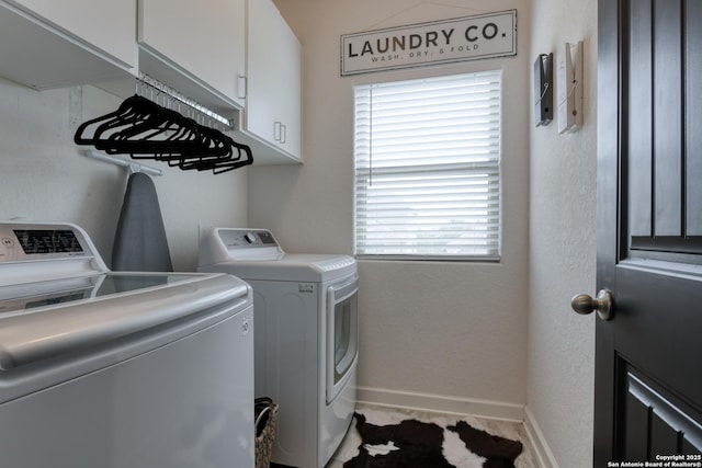 clothes washing area featuring cabinet space, baseboards, a textured wall, and washer and clothes dryer