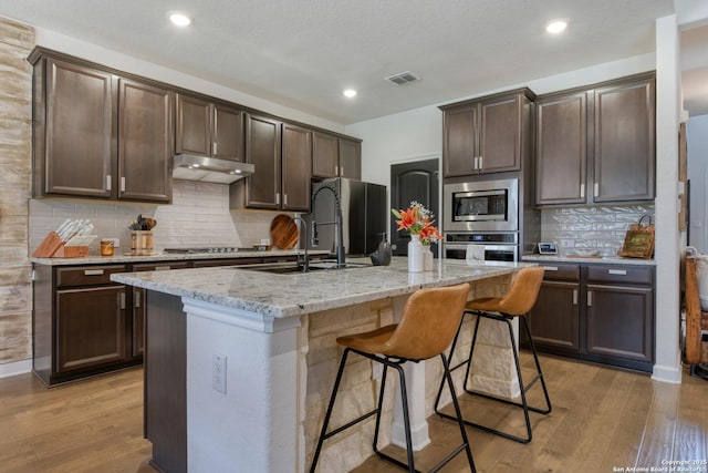 kitchen with visible vents, under cabinet range hood, dark brown cabinetry, and stainless steel appliances