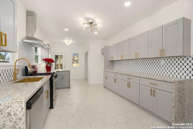kitchen featuring appliances with stainless steel finishes, a sink, wall chimney exhaust hood, tasteful backsplash, and gray cabinetry