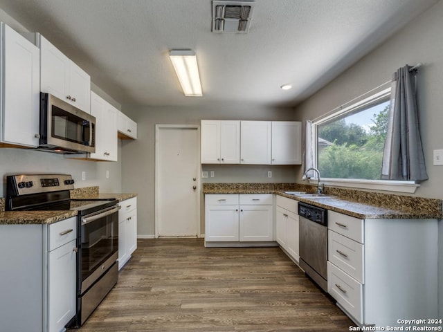 kitchen with white cabinets, a sink, dark wood finished floors, stainless steel appliances, and visible vents