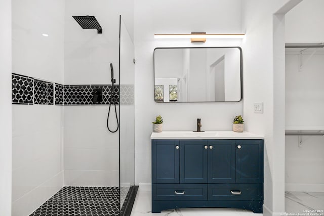 full bathroom with vanity, marble finish floor, baseboards, a spacious closet, and a tile shower