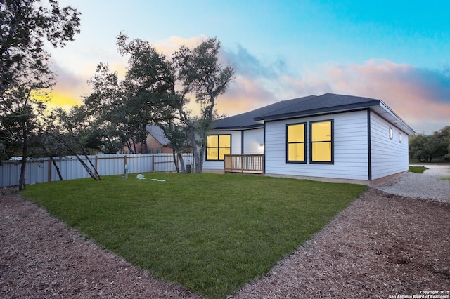 back of house featuring a lawn, roof with shingles, and fence
