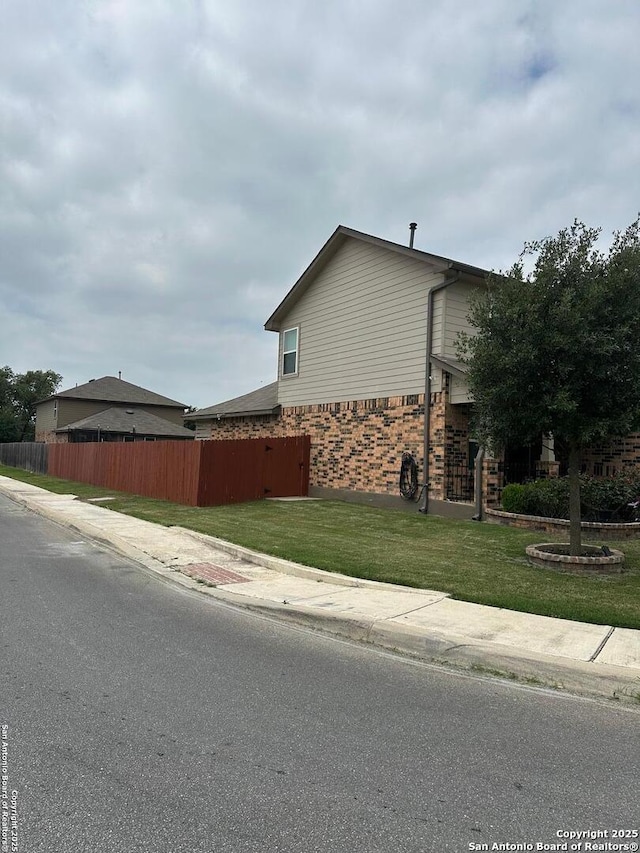 view of side of property with brick siding, a lawn, and fence