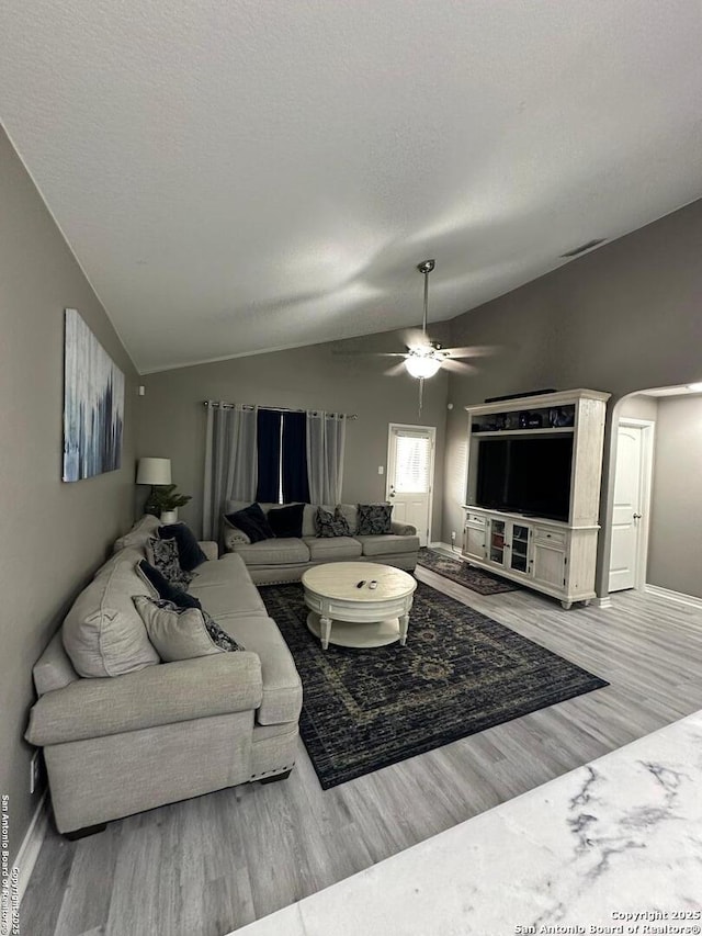 living area featuring arched walkways, a ceiling fan, baseboards, wood finished floors, and lofted ceiling