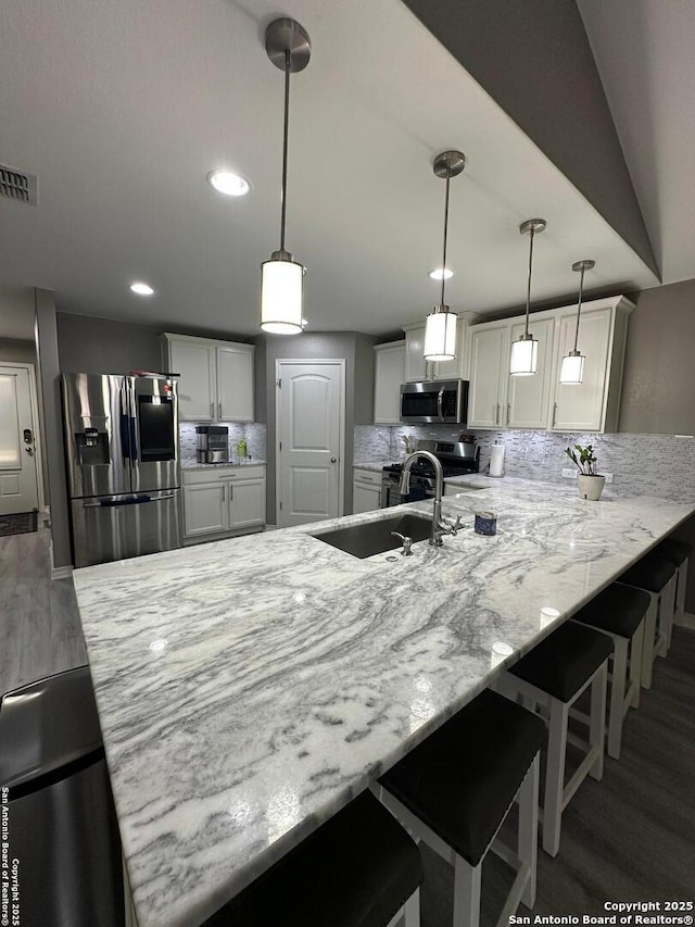 kitchen with a sink, stainless steel appliances, wood finished floors, tasteful backsplash, and visible vents