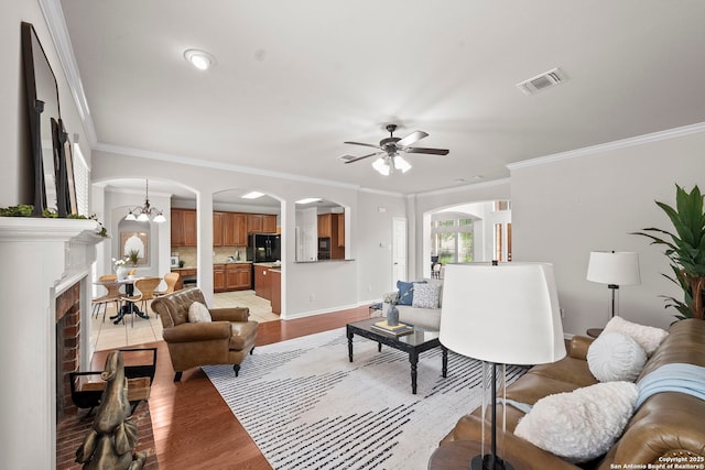 8715 Anton Chico, Helotes, TX 78023 - living room with visible vents, crown molding, arched walkways, ceiling fan with notable chandelier, and light wood-style flooring