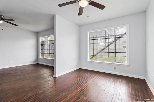 empty room featuring dark wood-type flooring, a ceiling fan, and baseboards