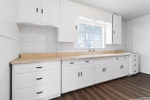 kitchen with light countertops, white cabinetry, dark wood finished floors, and a sink