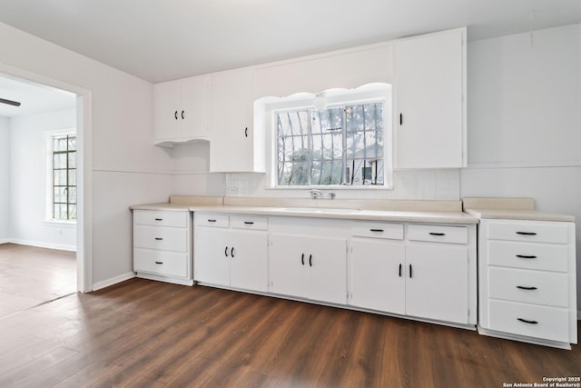 kitchen with a sink, light countertops, white cabinets, and dark wood-type flooring