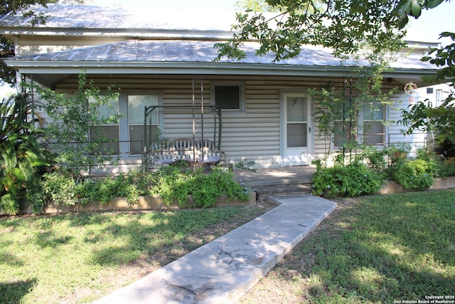 view of exterior entry with covered porch, a yard, and metal roof