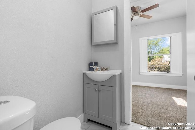 half bath with toilet, ceiling fan, baseboards, and vanity