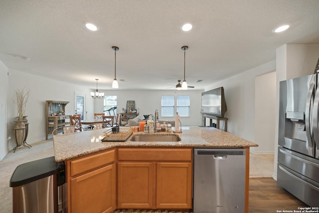 kitchen featuring pendant lighting, appliances with stainless steel finishes, light stone countertops, a sink, and open floor plan