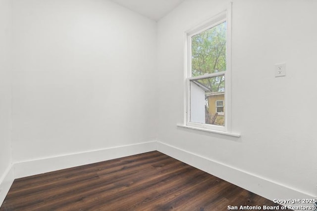 spare room with baseboards and dark wood-style flooring