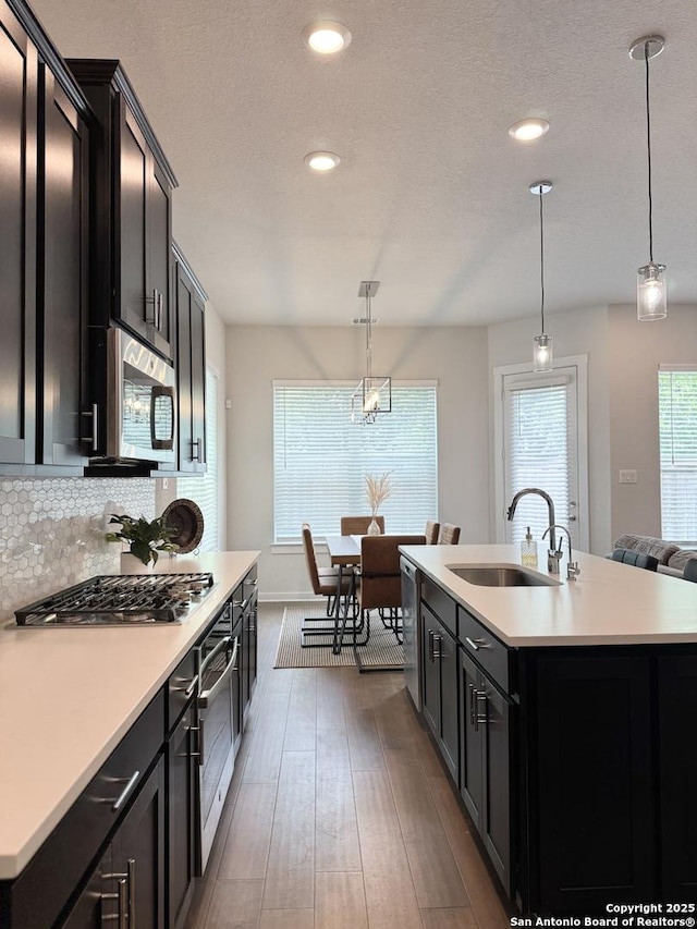 kitchen featuring appliances with stainless steel finishes, a sink, light countertops, dark cabinets, and dark wood-type flooring