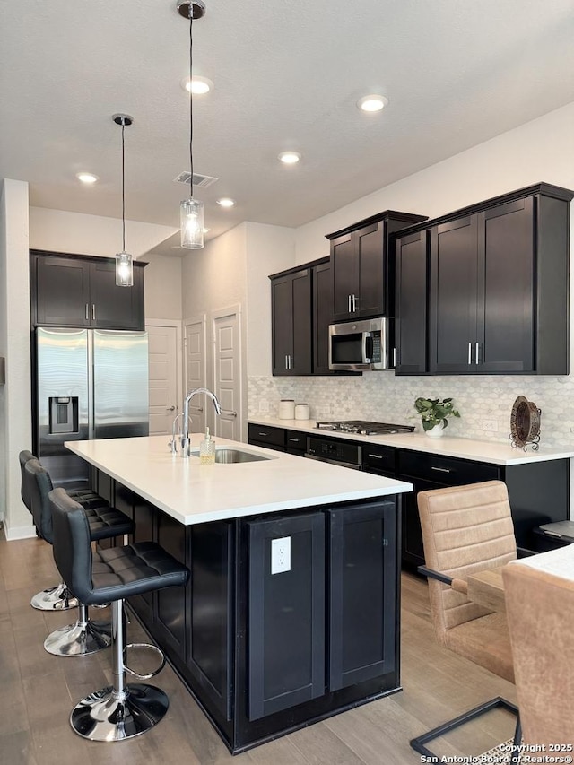 kitchen with a sink, a kitchen island with sink, backsplash, and stainless steel appliances