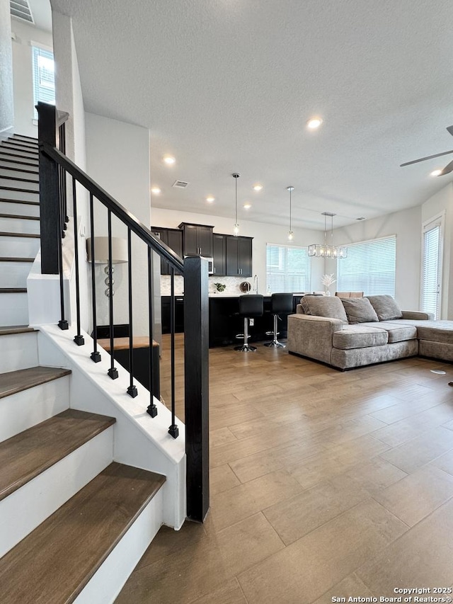 living area with recessed lighting, a textured ceiling, stairs, and ceiling fan with notable chandelier