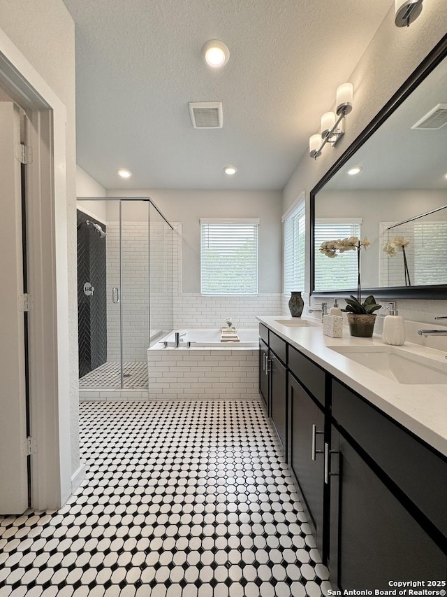 full bath featuring visible vents, double vanity, a bath, a shower stall, and a sink
