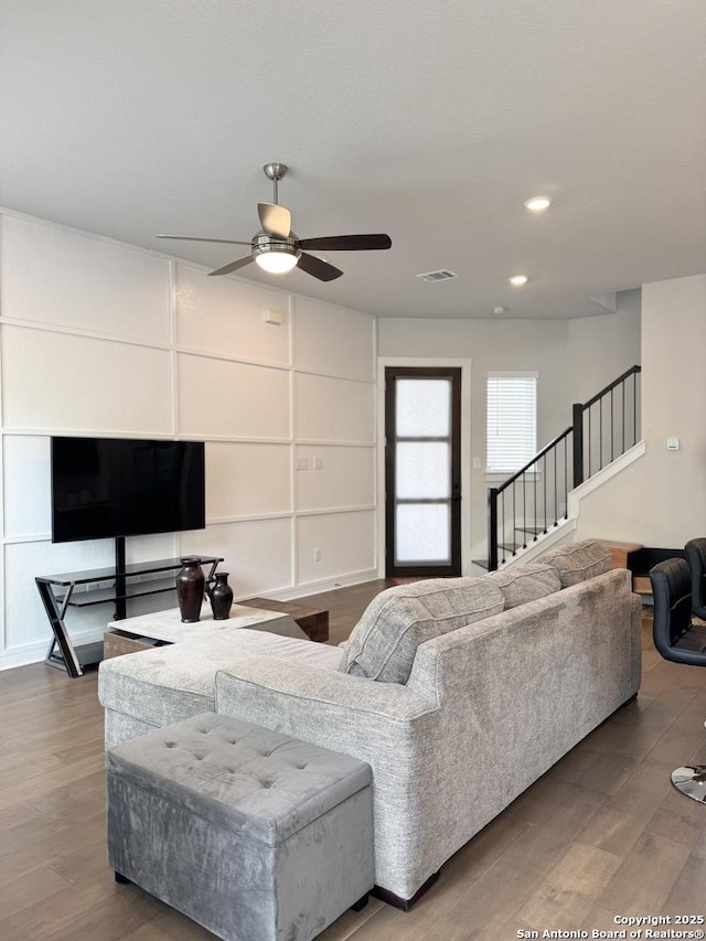 living room with a ceiling fan, visible vents, wood finished floors, and stairway
