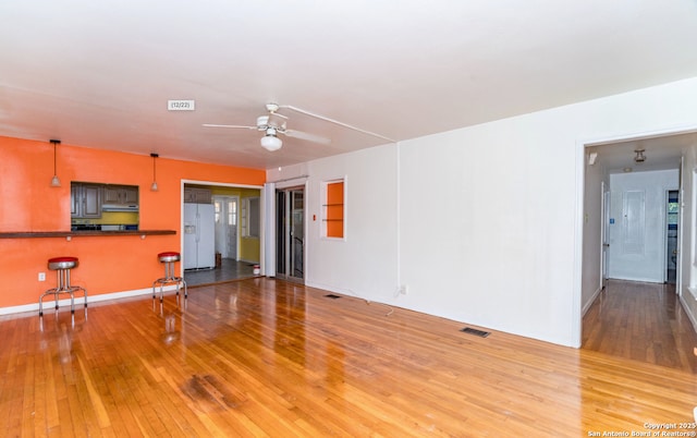 unfurnished living room with visible vents, baseboards, ceiling fan, and hardwood / wood-style floors