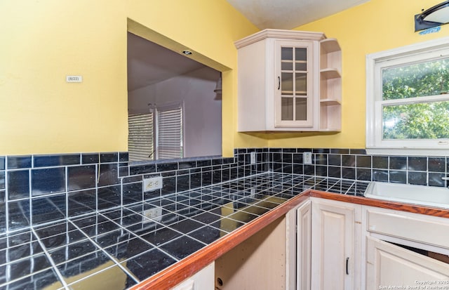 416 Alexander Hamilton, San Antonio, TX 78228 - kitchen featuring backsplash, glass insert cabinets, a sink, tile counters, and white cabinetry