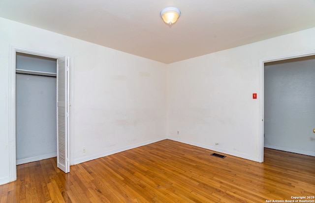 unfurnished bedroom featuring baseboards, a closet, hardwood / wood-style floors, and visible vents