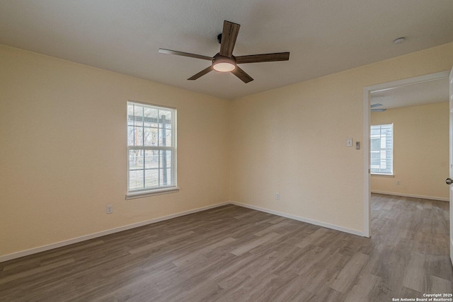 empty room with baseboards, a ceiling fan, wood finished floors, and a healthy amount of sunlight