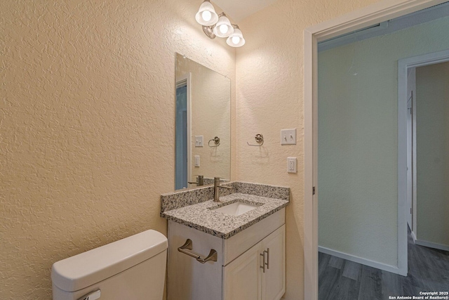 half bathroom featuring toilet, a textured wall, wood finished floors, and vanity