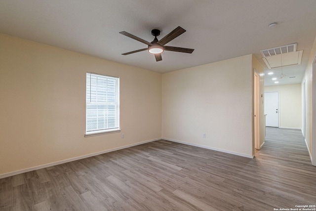 empty room featuring visible vents, wood finished floors, baseboards, attic access, and a ceiling fan