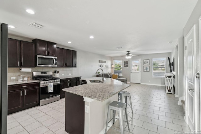 kitchen with ceiling fan, appliances with stainless steel finishes, a breakfast bar, a sink, and decorative backsplash