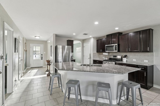 kitchen featuring a kitchen island with sink, a kitchen breakfast bar, arched walkways, a sink, and stainless steel appliances
