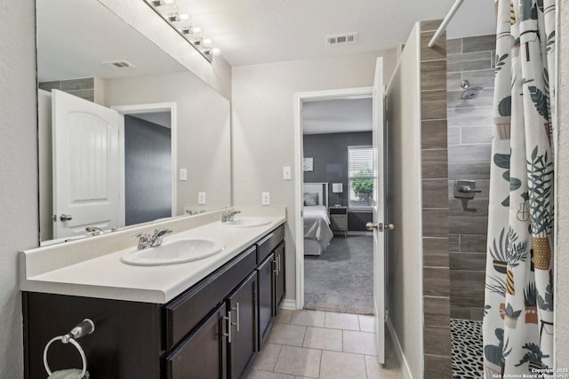 ensuite bathroom featuring a sink, a tile shower, double vanity, and visible vents