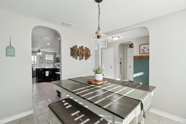 dining space with a ceiling fan, visible vents, arched walkways, light tile patterned floors, and baseboards