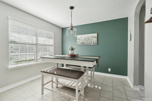 dining space with light tile patterned flooring, baseboards, and arched walkways