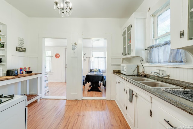 kitchen with dark countertops, white microwave, white cabinets, a sink, and light wood-style flooring