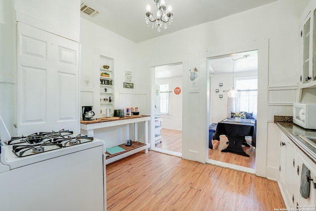 kitchen with white appliances, white cabinets, a chandelier, and light wood-style flooring