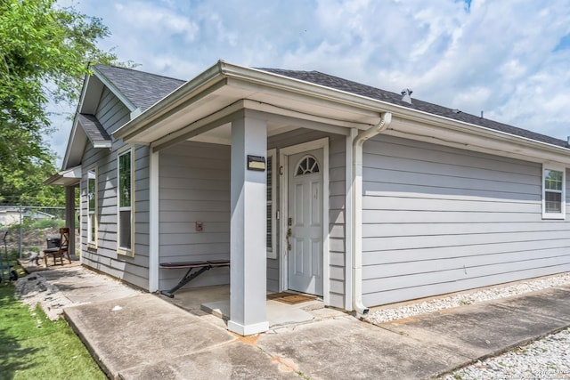 property entrance featuring roof with shingles and fence
