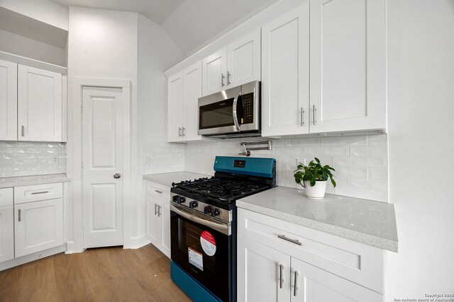 25 Main, Hempstead, TX 77445 - kitchen featuring light stone countertops, light wood-type flooring, white cabinets, tasteful backsplash, and appliances with stainless steel finishes
