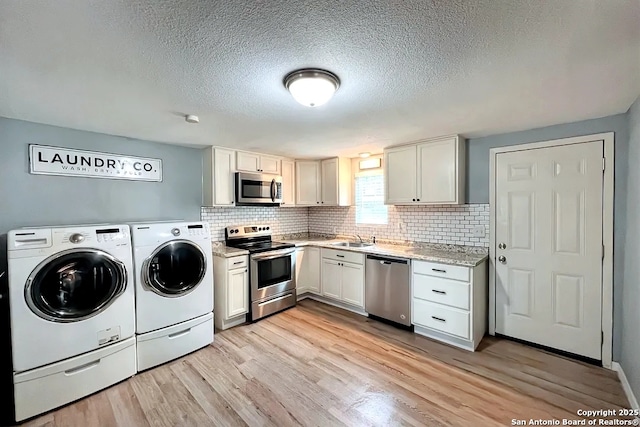 kitchen featuring light wood-style flooring, appliances with stainless steel finishes, washing machine and dryer, and tasteful backsplash