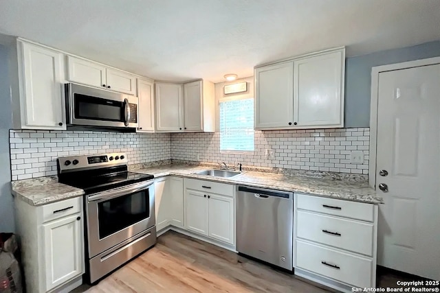 kitchen with a sink, light wood-style flooring, stainless steel appliances, white cabinetry, and tasteful backsplash