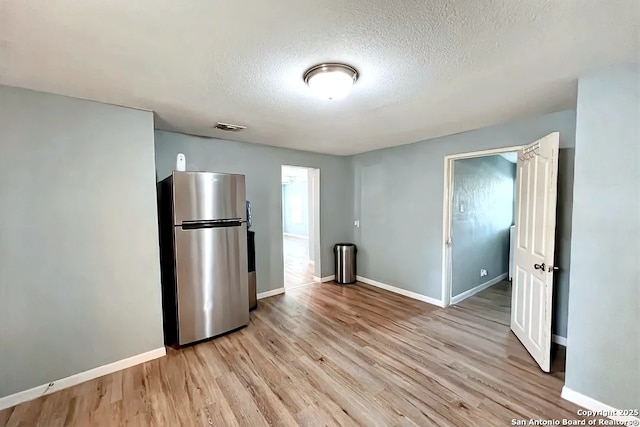 interior space featuring visible vents, a textured ceiling, light wood-style flooring, and baseboards
