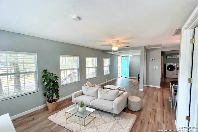 living area featuring baseboards, ceiling fan, washer and clothes dryer, and light wood-style flooring