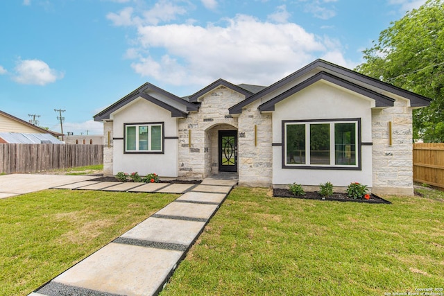 view of front facade featuring stucco siding, fence, a front yard, and stone siding