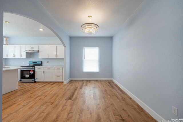 unfurnished dining area with an inviting chandelier, arched walkways, baseboards, and light wood-type flooring