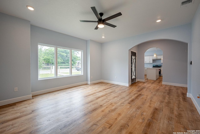 spare room with visible vents, baseboards, light wood-type flooring, arched walkways, and a ceiling fan