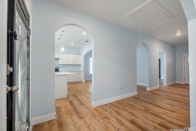 unfurnished room with arched walkways, baseboards, light wood finished floors, and attic access