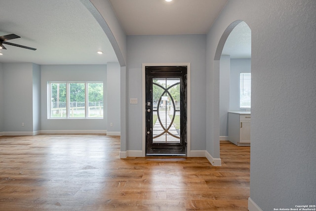 foyer featuring arched walkways, ceiling fan, light wood finished floors, and a wealth of natural light