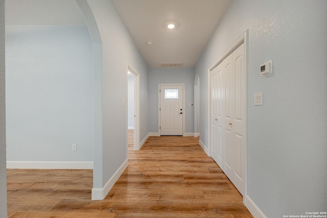 hallway featuring arched walkways, baseboards, light wood-type flooring, and visible vents