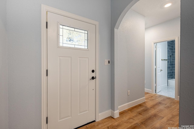 foyer with baseboards, arched walkways, and light wood finished floors
