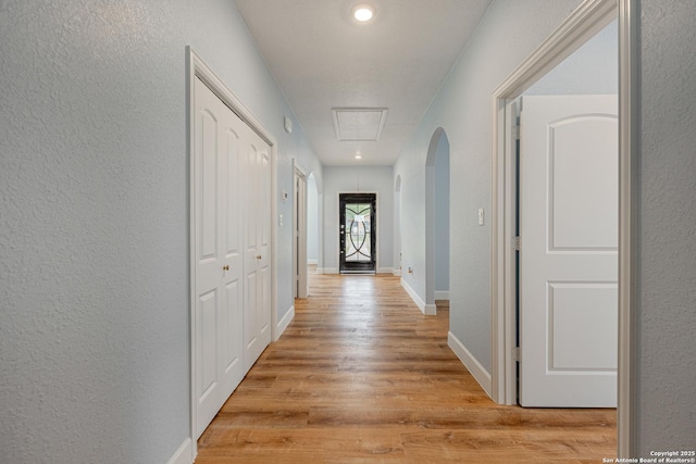hall featuring arched walkways, a textured wall, attic access, and light wood-style floors